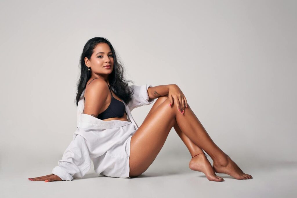 Confident woman in black bikini and white shirt posing elegantly in studio setting.