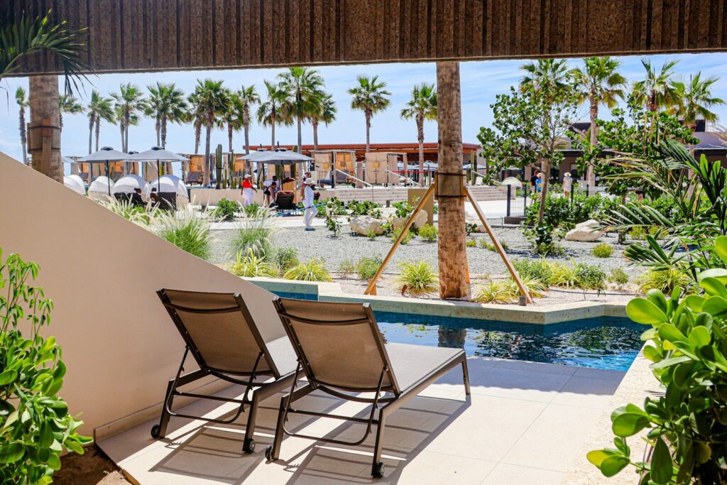Two lounge chairs by a small pool with palm trees.