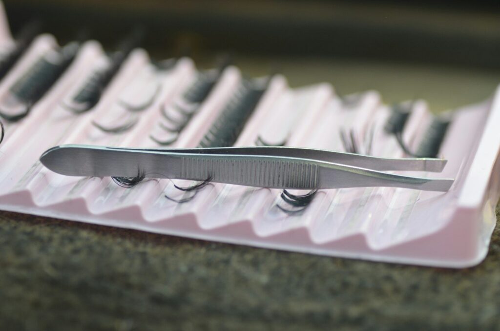 Tweezers resting on a tray of false eyelashes