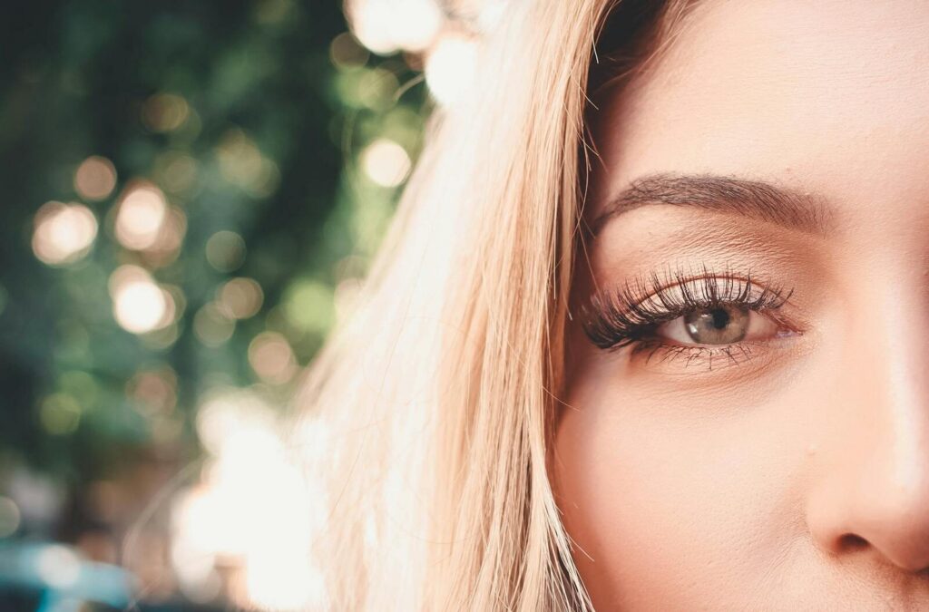 Detailed close-up of a woman's eye showcasing long eyelashes and eyebrow outdoors.