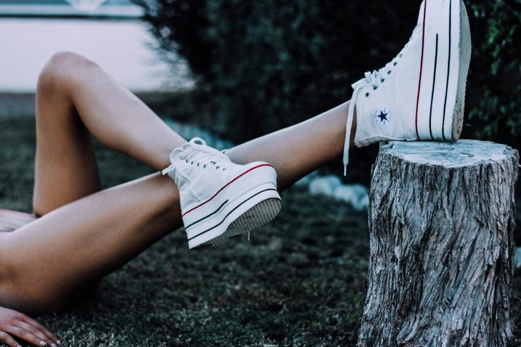 Crop anonymous female lying on grassy ground in forest with crossed bare legs on tree stub