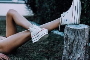 Crop anonymous female lying on grassy ground in forest with crossed bare legs on tree stub