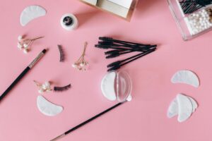 Aesthetic makeup tools and beauty items arranged on a pink surface.